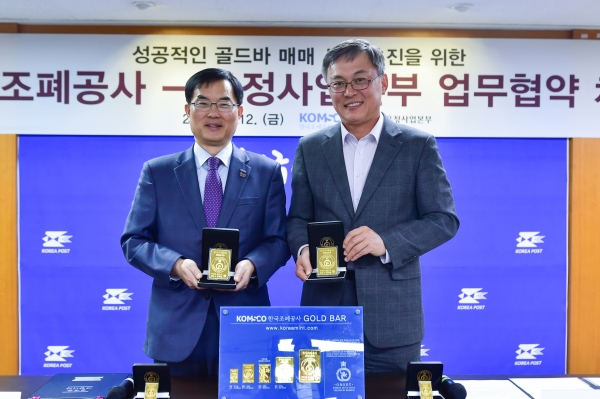 조용만 조폐공사 사장(사진 왼쪽)과 강성주 우정사업본부장이 업무협약을 체결한 후 ‘오롯 골드바’를 들어 보이고 있다