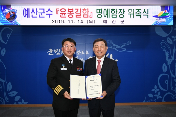 황선봉 예산군수(사진 오른쪽)가 윤봉길함 박순식 해군대령으로부터 명예함장으로 위촉받는 모습
