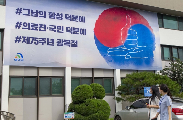대덕구청을 방문한 시민들이 청사 벽면에 게시된 대형 현수막를 바라보며 광복절 순국선열의 의미를 되새기고 코로나19 극복에 힘쓰는 의료진들에게 감사의 마음을 다지고 있다.]