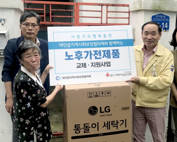 지난 18일 태안읍 지역사회보장협의체가 태안읍의 한 저소득 가정에 세탁기를 지원하고 있는 모습(패널 들고 있는 왼쪽 사업 대상자, 오른쪽 황용렬 태안읍장)