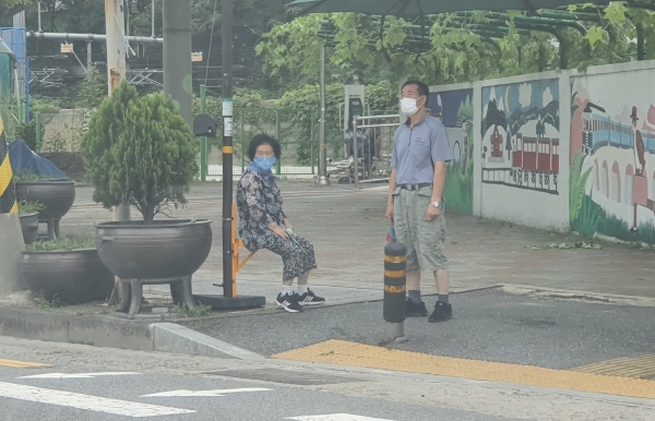주민이 횡단보도 옆 행복의자에 앉아서 신호를 기다리는 동안 쉬고 있다