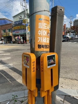 주민이 횡단보도 옆 행복의자에 앉아서 신호를 기다리는 동안 쉬고 있다