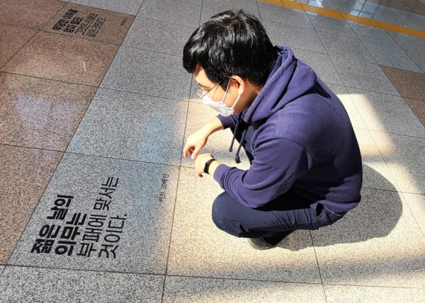 대전도시철도를 이용 중인 한 시민이 지족역 청렴 테마공간 바닥에 부착된     청렴명언을 살펴 보고 있다.
